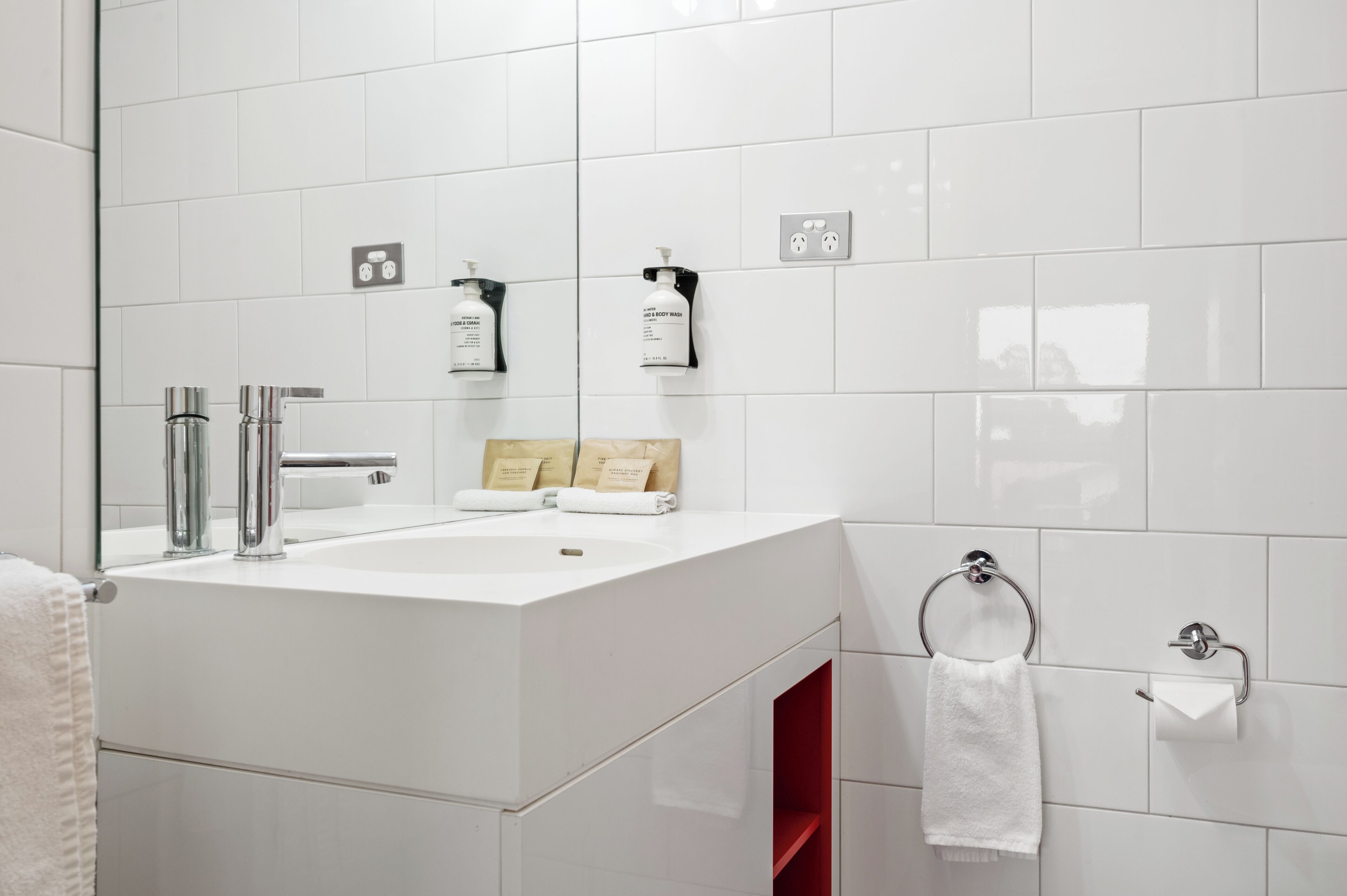 Un baño moderno con un lavamanos blanco, grifería cromada, un espejo y artículos de aseo en la pared.