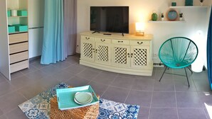 Ein modernes Wohnzimmer mit Fernseher, einem kleinen Tisch mit Schale, einem Sessel, einem Schrank und einem Regal mit Dekoration.