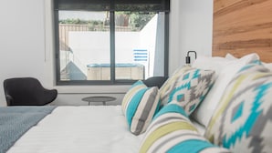 Un dormitorio con cama, una silla, una mesita y una ventana con vistas al exterior.