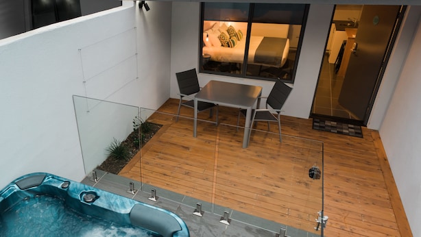 Un patio exterior moderno con un jacuzzi, una mesa de comedor con sillas y vista a una zona de dormitorio.