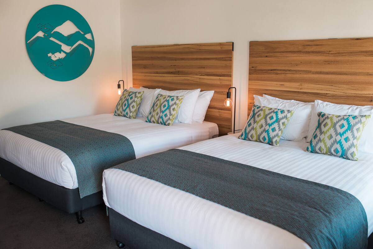 A hotel room with two beds, each with a wooden headboard, white bedding, and patterned pillows.