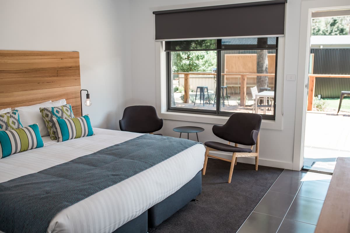 A modern bedroom with a large bed, two chairs, a small table, and a window with a view of the outdoors.