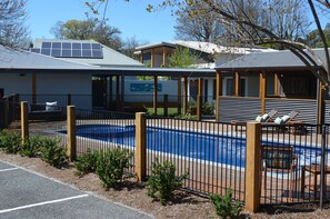 A pool area with a fenced deck, a covered seating area, and a building with a sign. - Bright Colonial Motel (Bright)