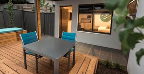A patio with a table and chairs, a wooden deck, and a view of a room with a bed and a window. - Bright Colonial Motel (Bright)