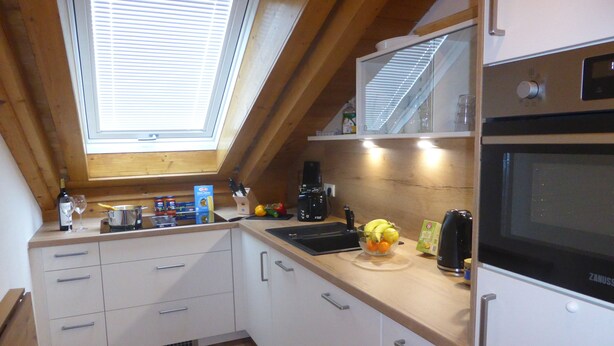A kitchen with a skylight, wooden ceiling, white cabinets, and a black oven.