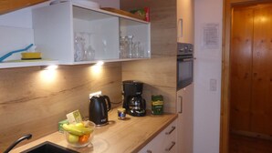 A kitchen with wooden cabinets, a coffee maker, a kettle, and a fruit bowl.