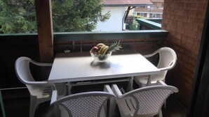 A balcony with a white table and chairs, a bowl of fruit, and a view of a building with a red roof.