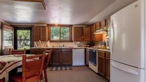 A kitchen with wooden cabinets, a white refrigerator, a coffee maker, and a dining table with chairs. - Private Cottage away from Crowds (Cody)