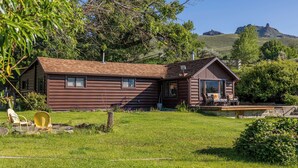 A rustic log cabin with a deck and a small pool, surrounded by lush greenery and hills in the background. - Private Cottage away from Crowds (Cody)
