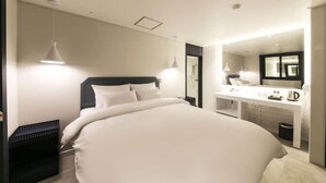 A modern hotel room with a large bed, a bedside table, a mirror, and a small desk with a lamp. - Sinan E.KKLIM Hotel (Gwangju)