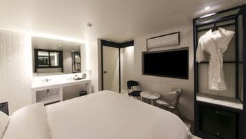 Una habitación de hotel moderna con una cama grande, un tocador con espejo, una bata colgada en la pared y un televisor de pantalla plana.
