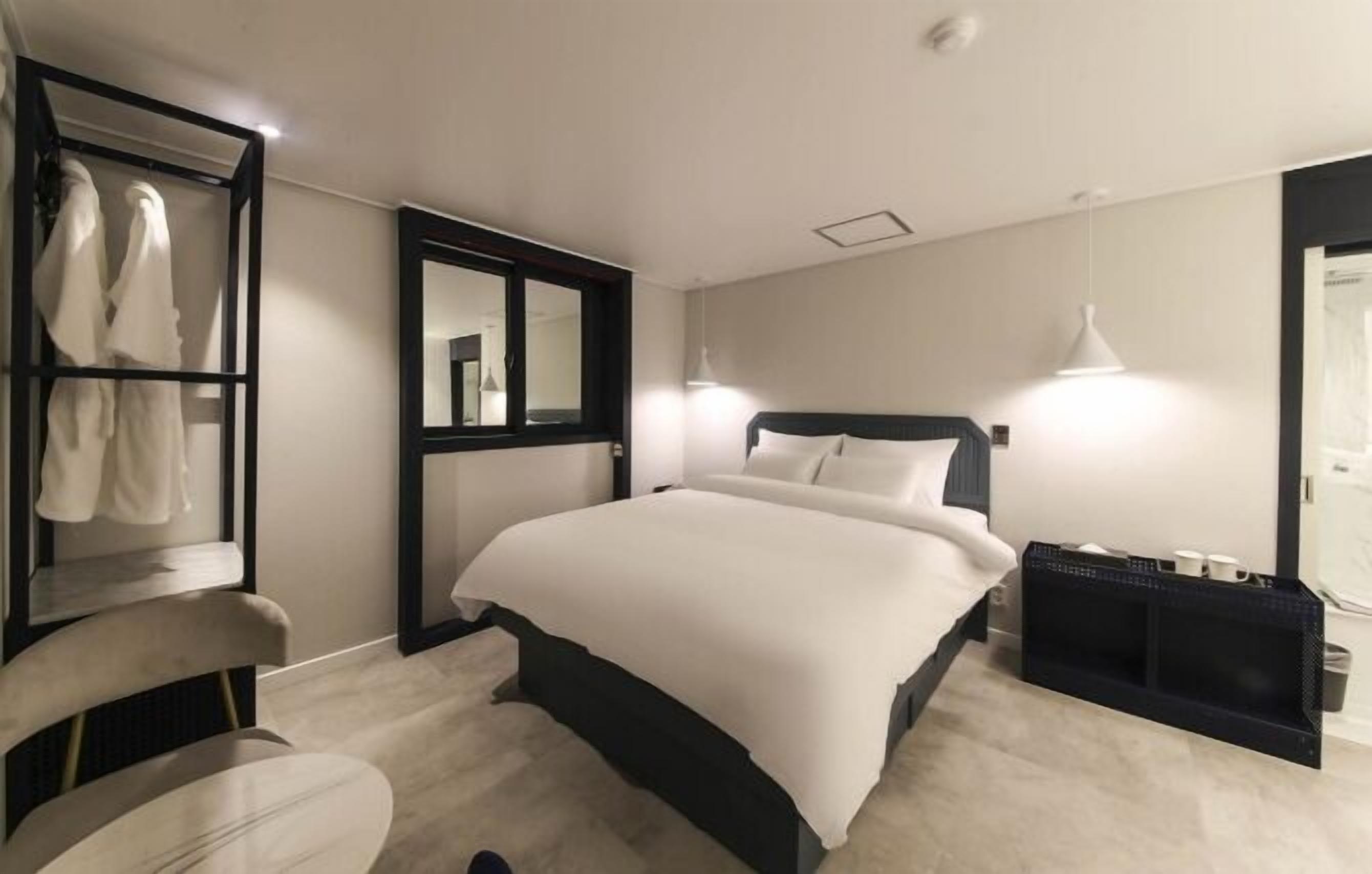 A modern hotel room with a large bed, a seating area with a chair, a wardrobe, and a mirror.