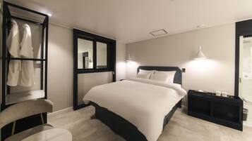 A modern hotel room with a large bed, a seating area with a chair, a wardrobe, and a mirror.