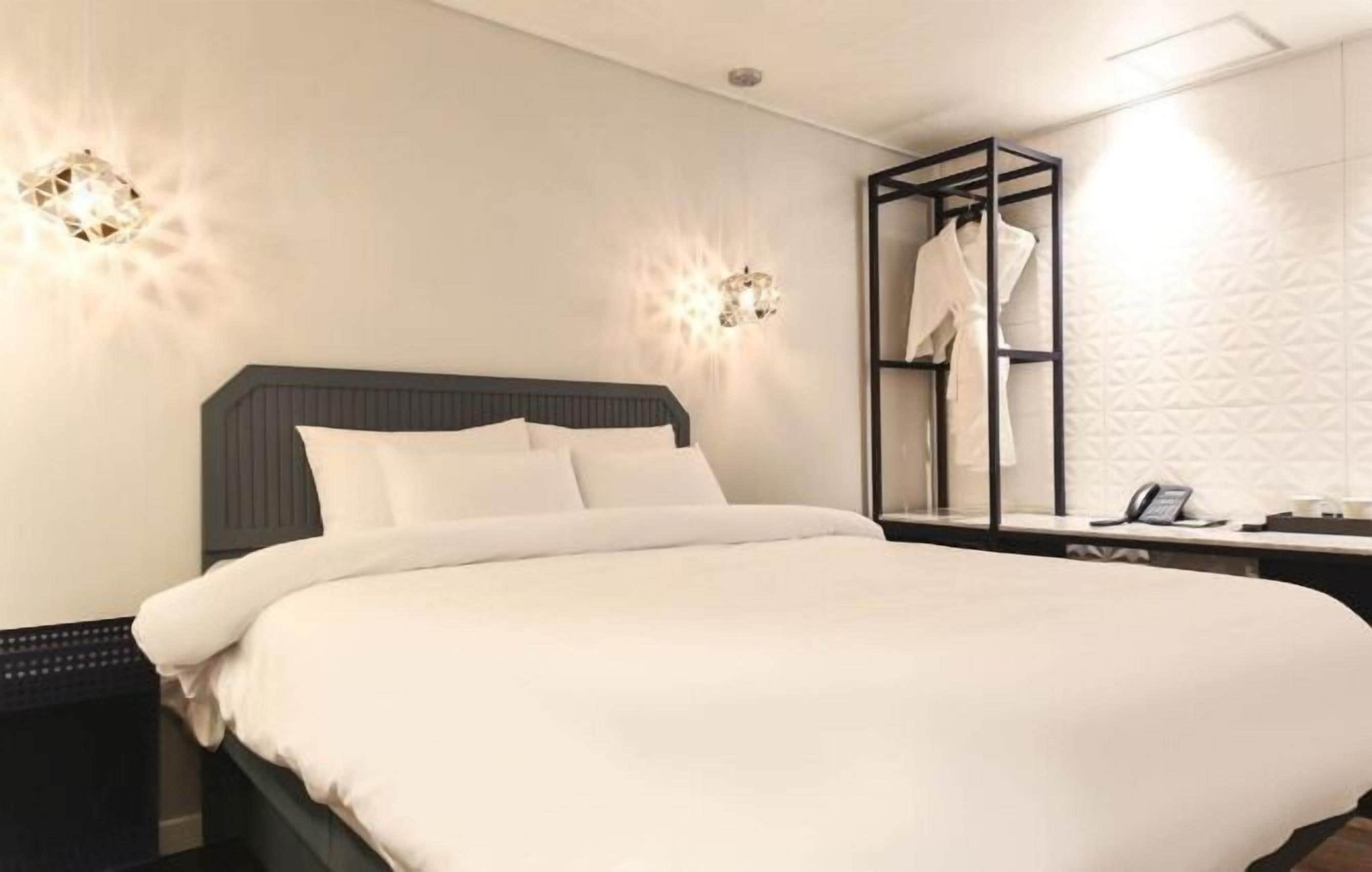 A neatly made bed with white linens, a dark headboard, and two wall-mounted sconces.