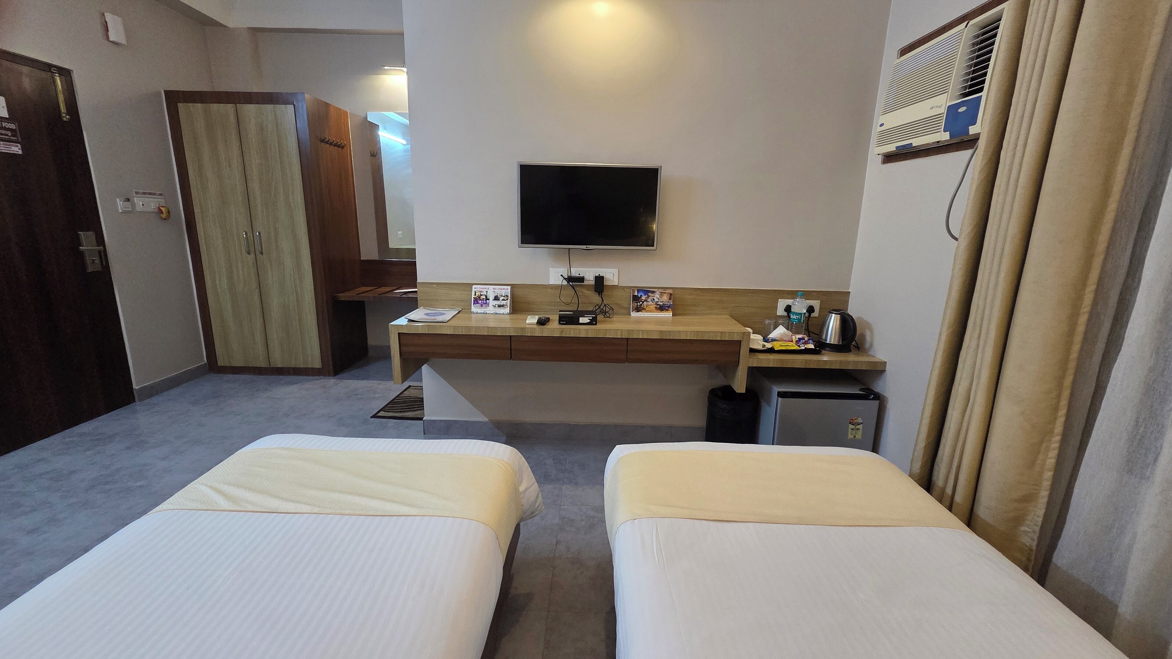 A hotel room with two beds, a desk with a flat-screen TV, a minibar, and a small refrigerator.