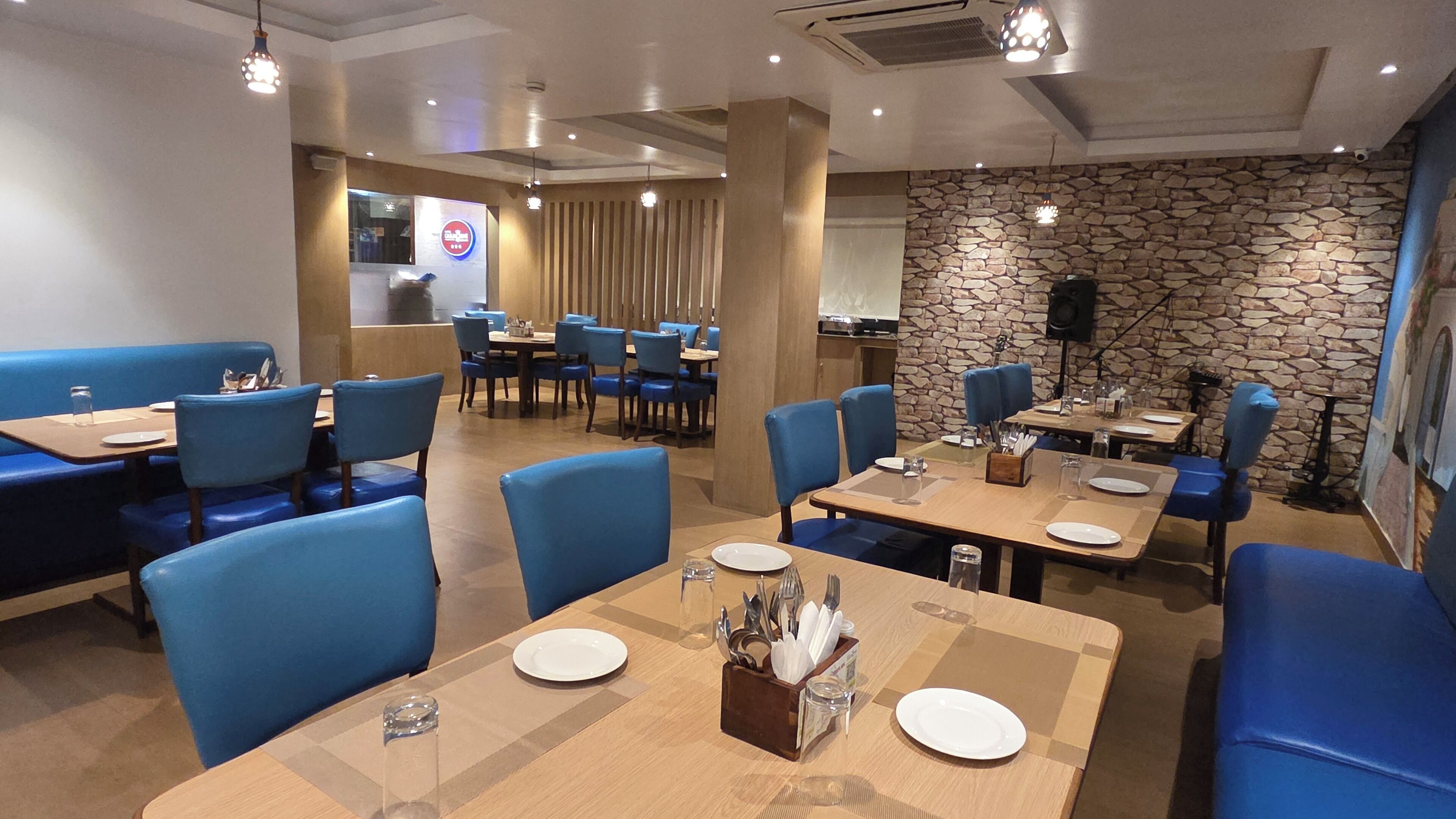 Interior de un restaurante con cabinas y mesas azules, detalles de pared de piedra y un logotipo visible en la pared.