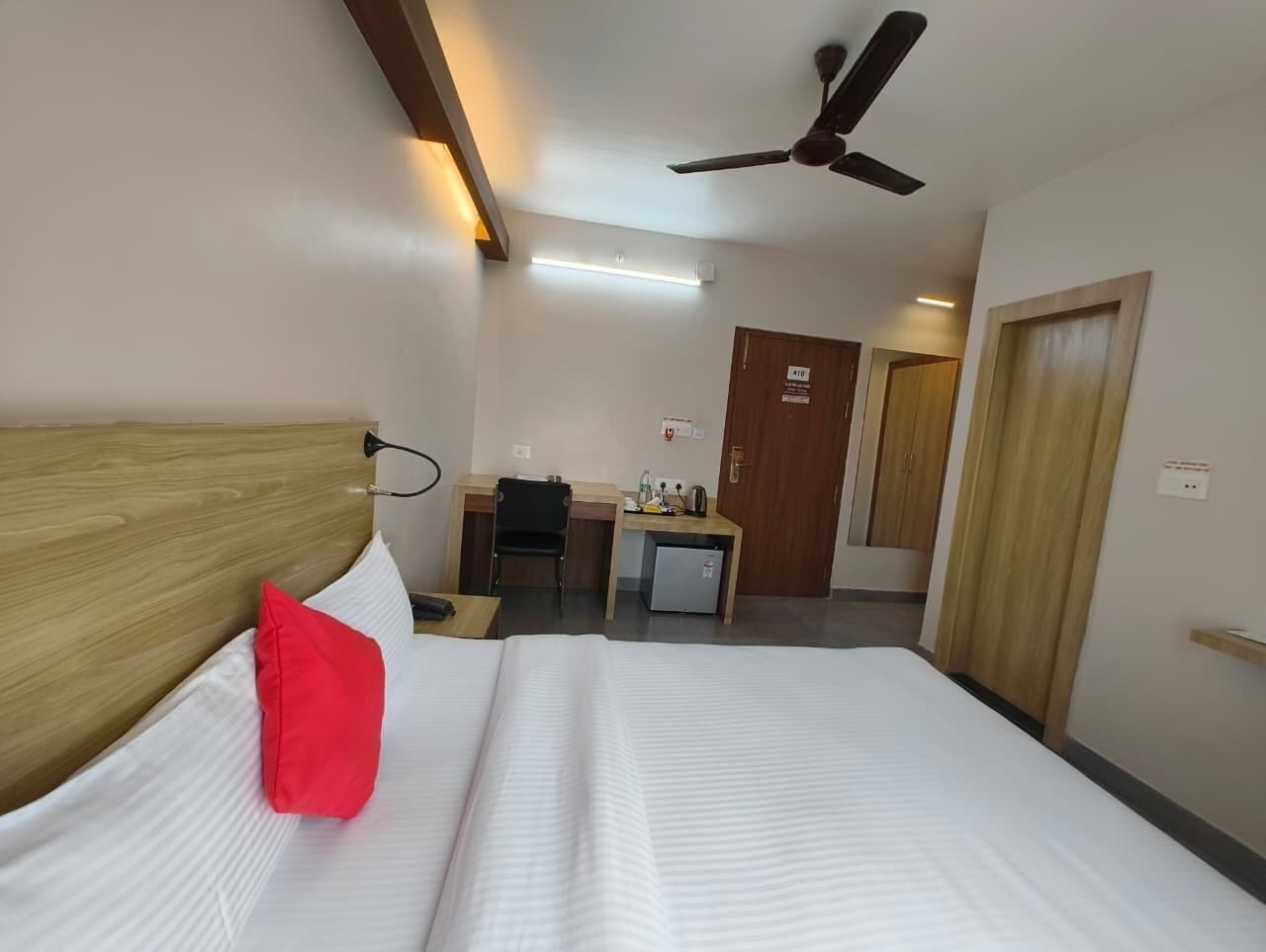 A hotel room with a bed, a desk, a chair, a ceiling fan, and a door.