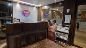 A hotel reception desk with a wooden counter, a sign for 'Hotel Gulmohar Grand', and a poster advertising a 'Musical Night'. - Hotel Gulmohar Grand (East Jorhat)