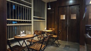 A dining area with wooden tables and chairs, a window with vertical blinds, and a door with a sign. - Hotel Gulmohar Grand (East Jorhat)
