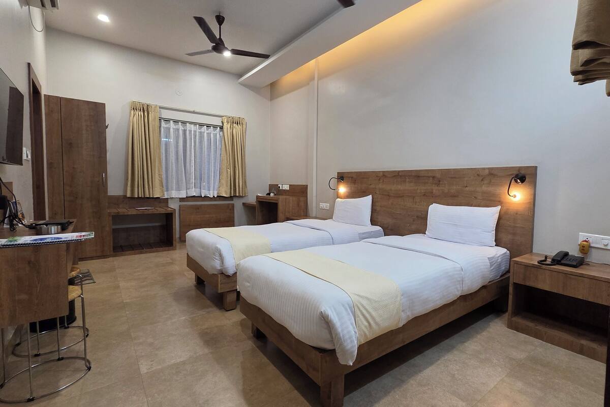 A hotel room with two beds, a desk, a TV, and a ceiling fan.