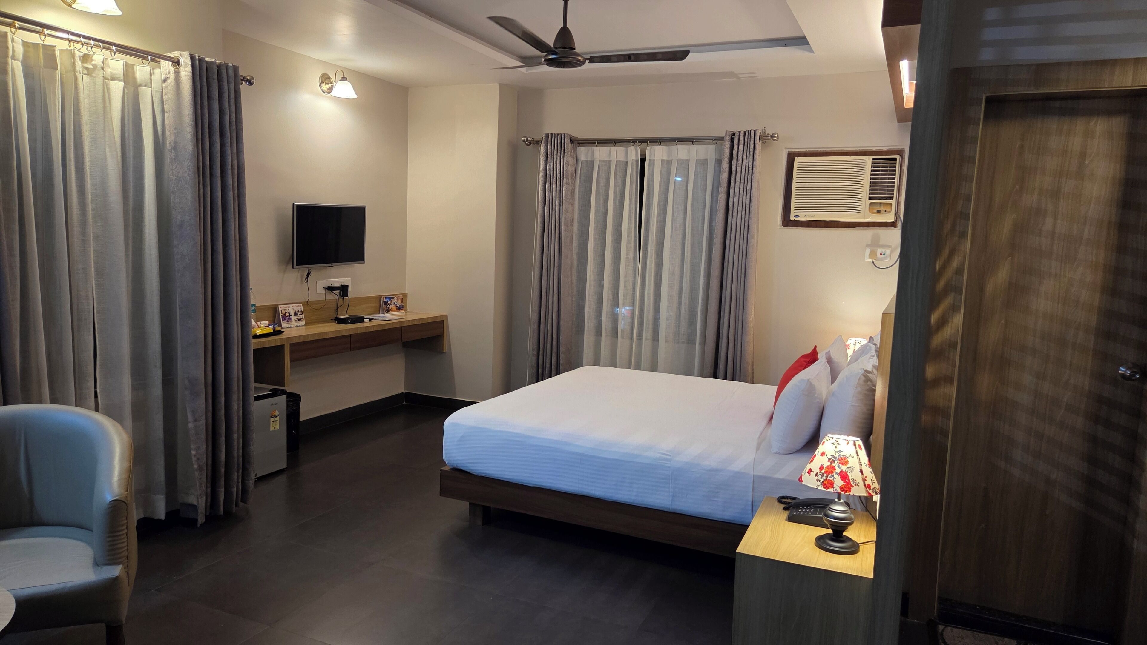 A hotel room with a bed, a desk, a chair, a TV, and a ceiling fan.