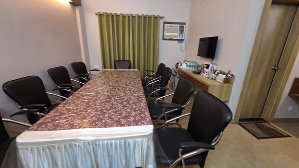 Un salón de conferencias con una larga mesa, sillas negras, un mostrador de recepción y un aire acondicionado instalado.