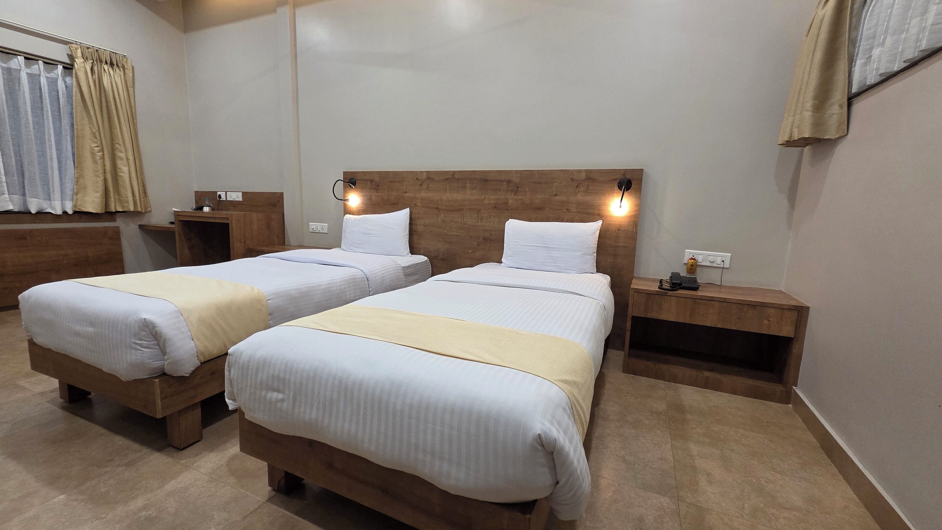 Habitación de hotel con dos camas, cabeceros de madera, mesitas de noche y un escritorio pequeño con una silla.