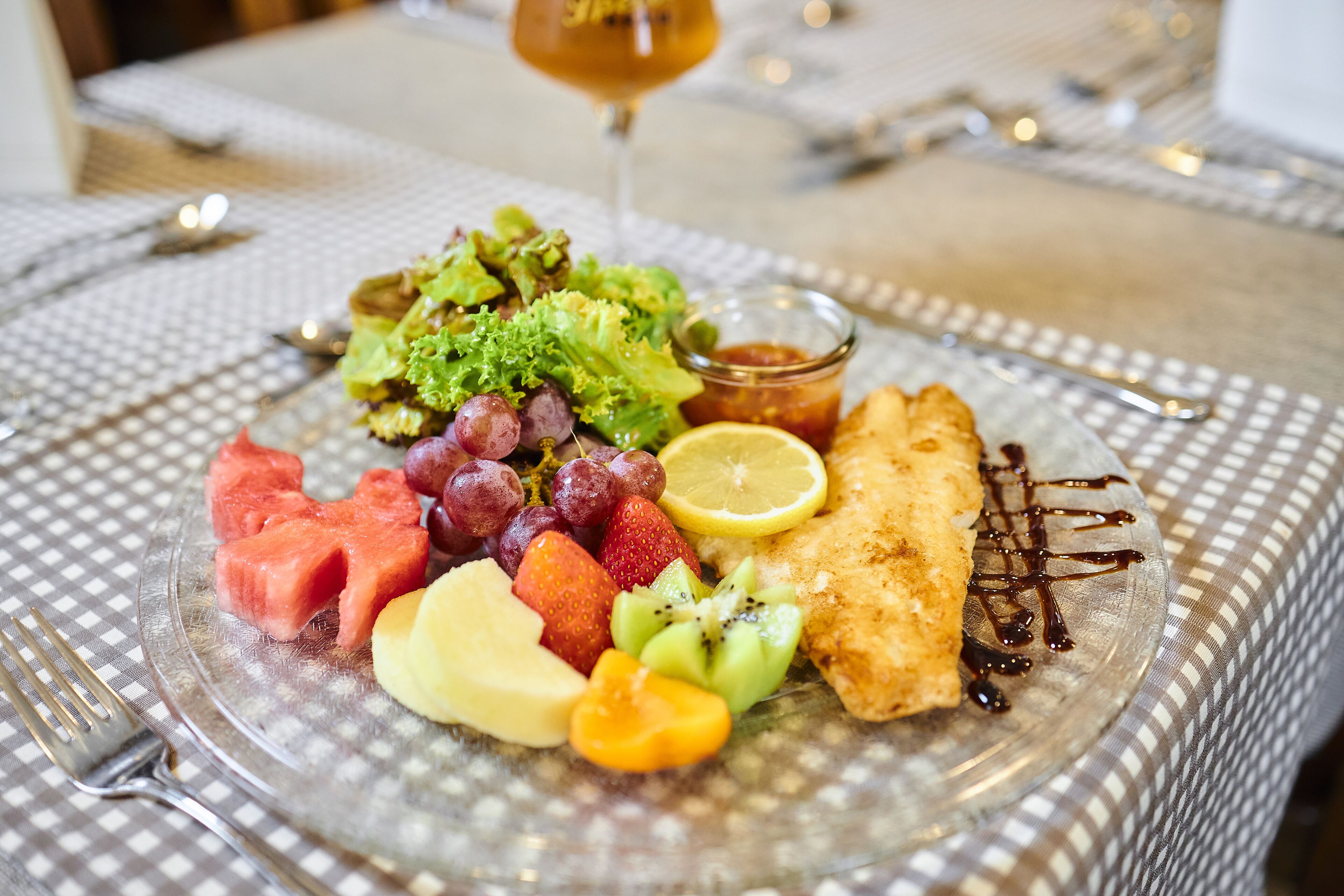 Ein Teller mit verschiedenen Früchten, einem Salat und einem Stück frittiertem Essen, dazu ein Glas Wein.