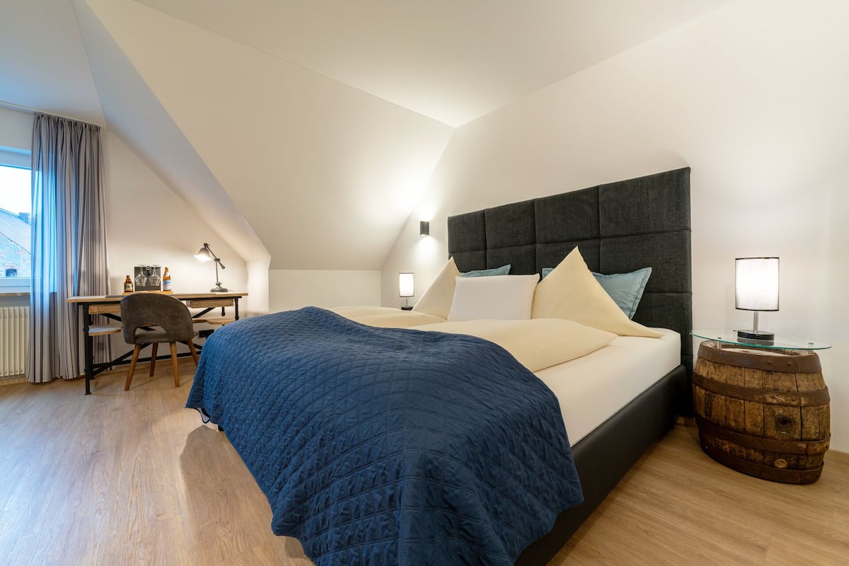 A bedroom with a bed, desk, chair, and a small table with a lamp.