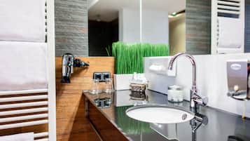 A modern bathroom with a glass sink, a chrome faucet, and a towel rack with white towels.