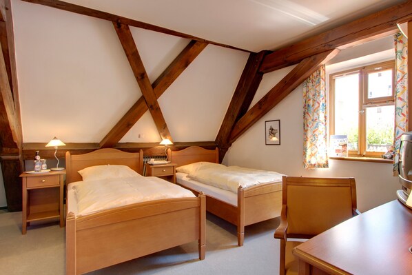 A room with two wooden beds, a wooden table, a chair, a lamp, and a window with curtains.