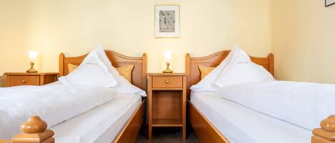 A hotel room with two wooden beds, white linens, nightstands with lamps, a framed picture on the wall, and a wooden floor.