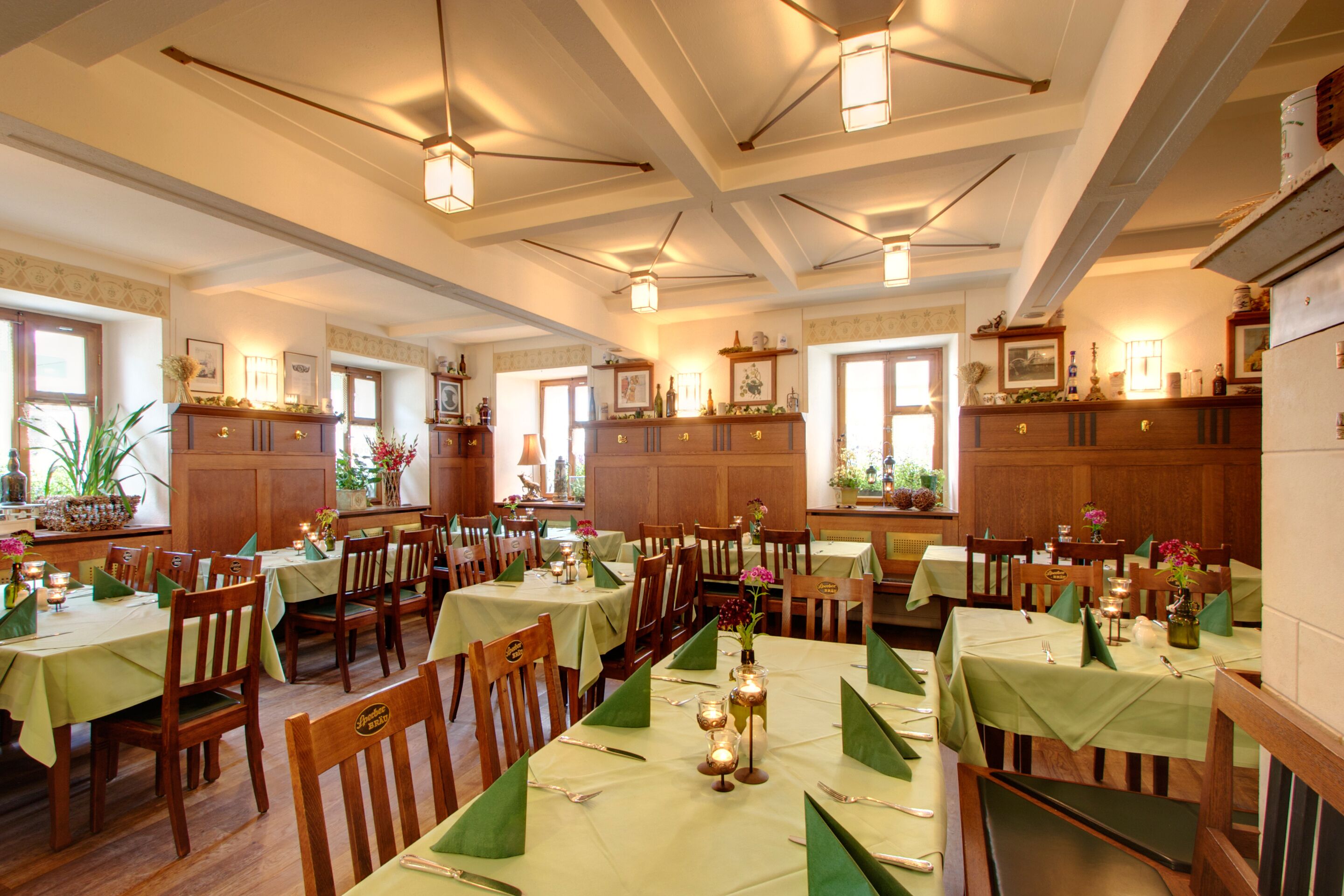 Un comedor con varias mesas dispuestas para el servicio, sillas de madera y manteles verdes.