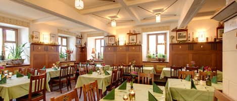 Un comedor con varias mesas dispuestas para el servicio, sillas de madera y manteles verdes.