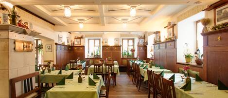 A restaurant with multiple tables and chairs, wooden paneling, and framed pictures on the walls.