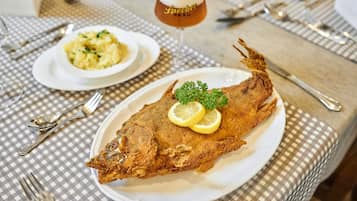 A dining table with a plate of fried fish, a glass of beer, and a bowl of mashed potatoes.