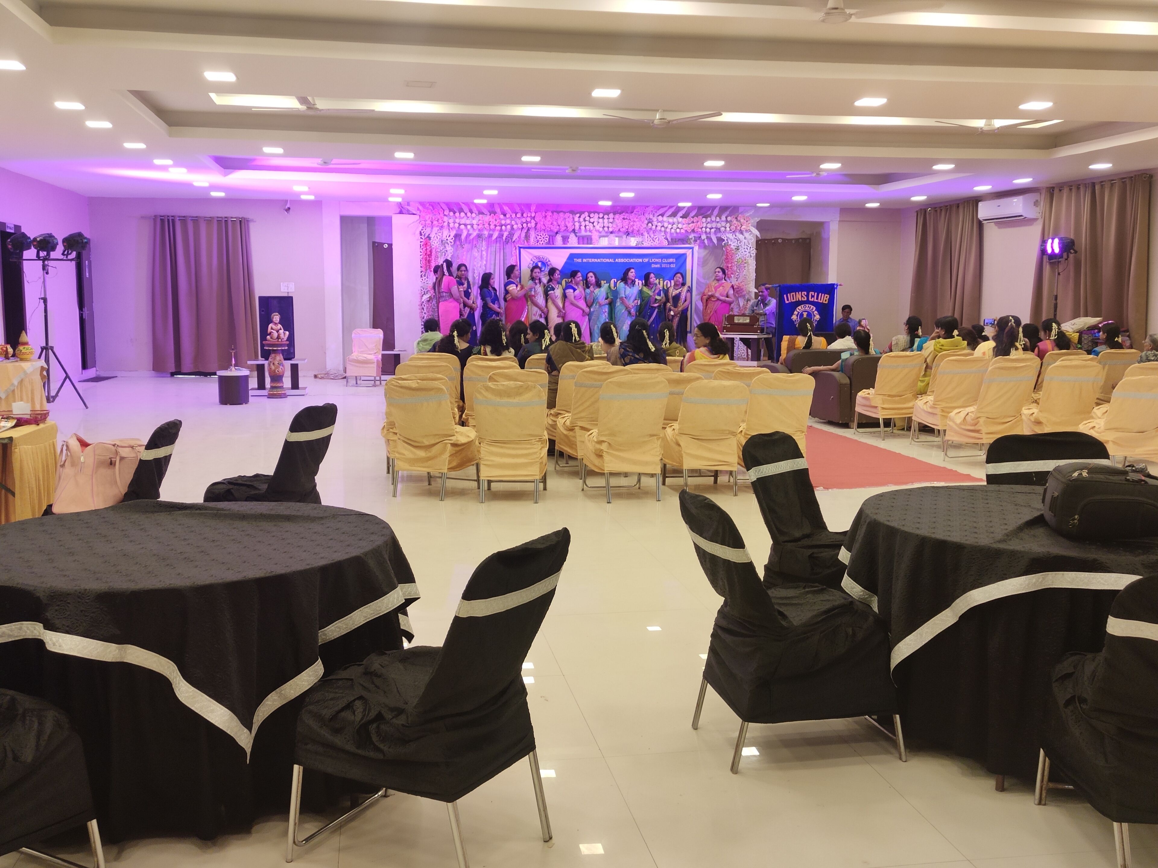 A conference room with rows of chairs, a stage with a banner, and a ceiling fan.