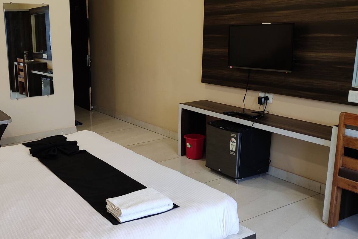 Quarto de hotel com cama, escrivaninha, televisão e espelho.