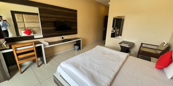 Habitación de hotel con cama, escritorio, silla, televisor montado en la pared y espejo.