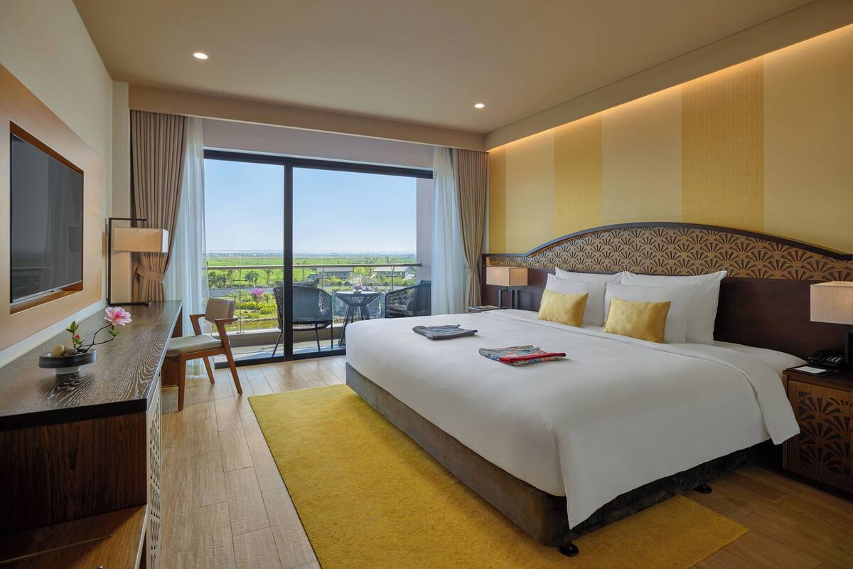 Ein Hotelzimmer mit einem großen Bett, einem Schreibtisch mit Stuhl, Blick ins Freie und einem Balkon.