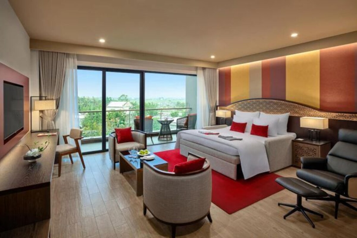 Quarto de hotel com cama, escrivaninha, cadeira, sofá, televisão e varanda com vista.