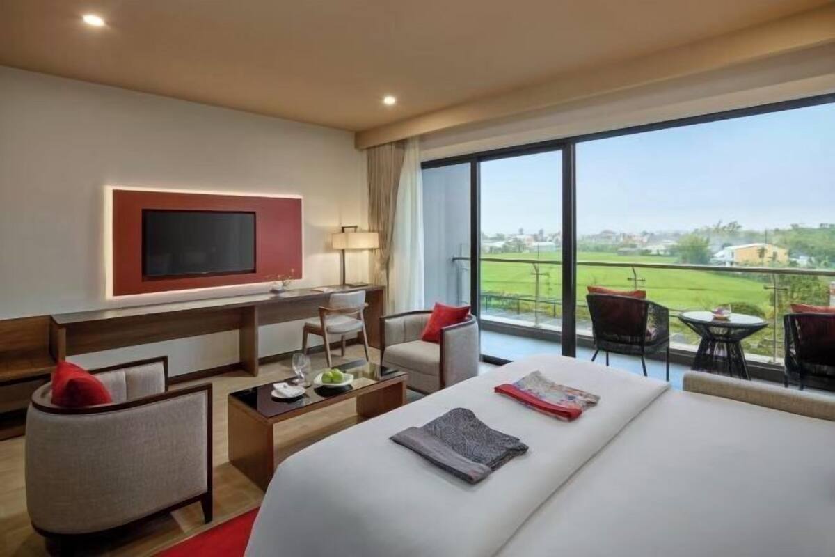 Ein Hotelzimmer mit einem großen Bett, einem Schreibtisch, einem Fernseher und einem Balkon mit Sitzgelegenheiten.