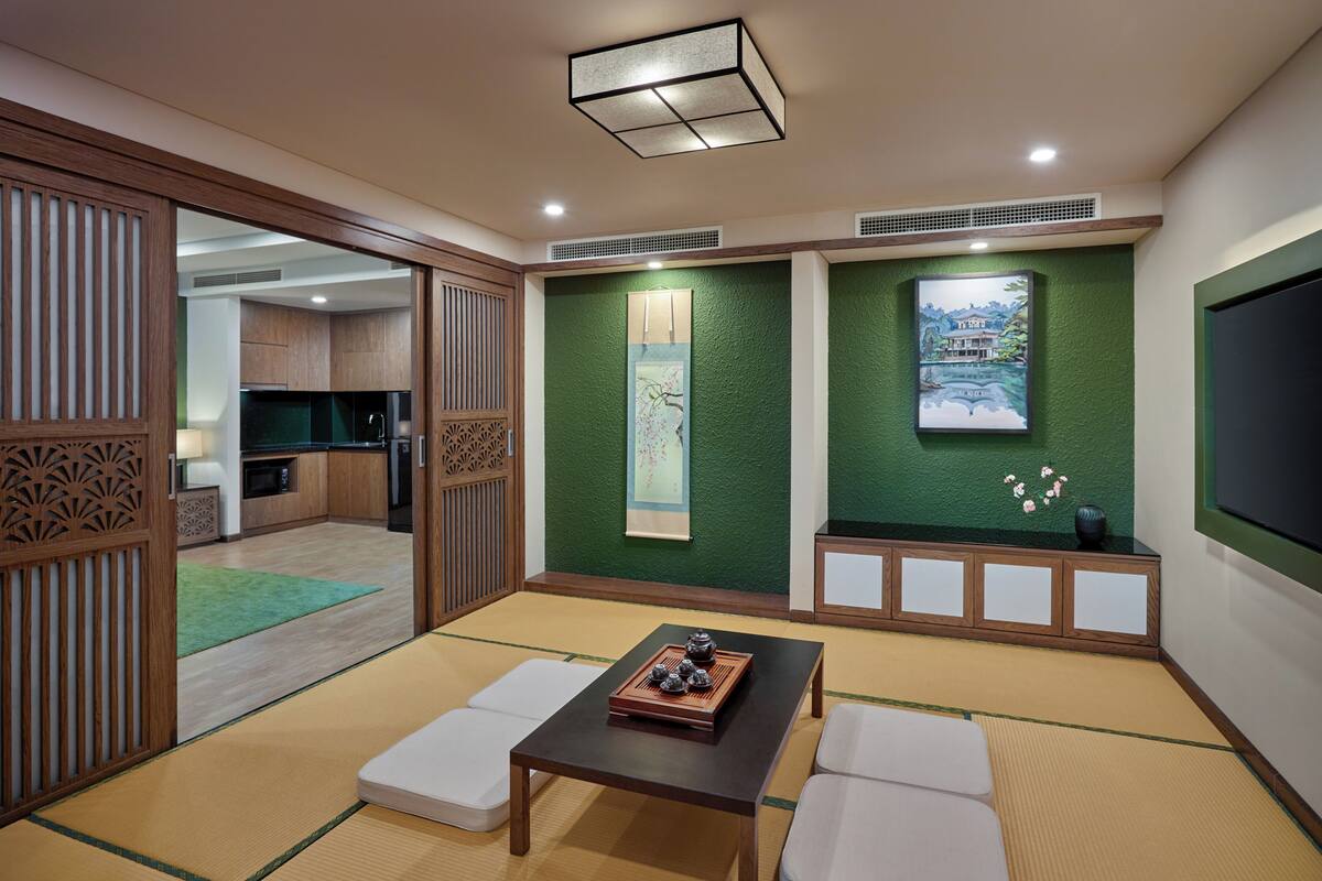 Ein traditioneller japanischer Raum mit Tatami-Boden, einem niedrigen Tisch mit Teeset und Schiebetüren zu einer Küche.
