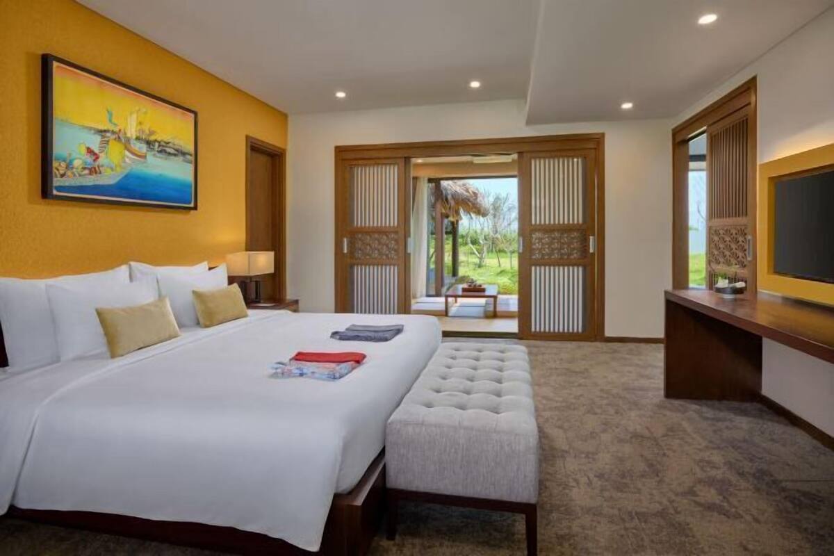 Ein Hotelzimmer mit einem großen Bett, einer Bank, einem Schreibtisch und einem Gemälde an der Wand.