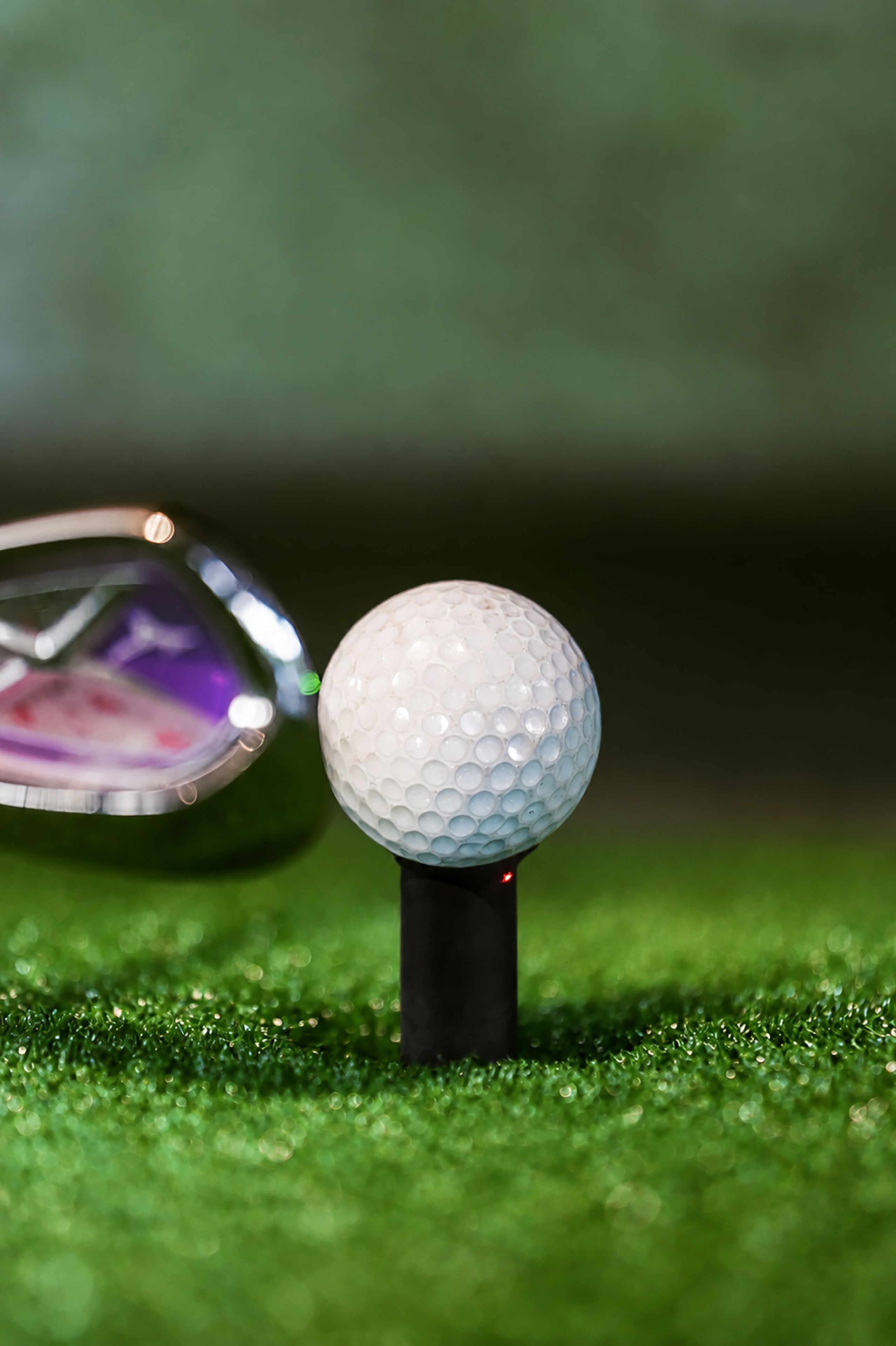 A golf ball on a tee on artificial grass.