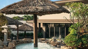 A pool area with a person in the water, surrounded by rocks and a thatched umbrella.