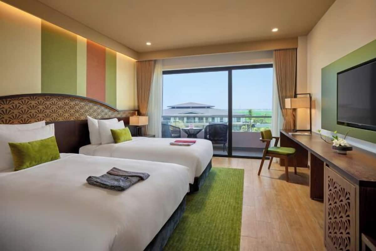 A hotel room with two beds, a desk, a television, and a view of the outside.