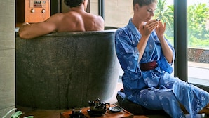 A room with a large window, a wooden bench, and a traditional Japanese tea set.