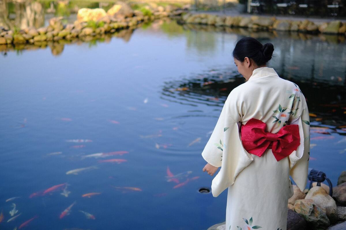 Eine Person in traditioneller Kleidung steht an einem ruhigen Gewässer mit Fischen.