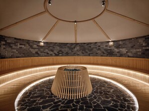 A circular wooden bench with a central pole, surrounded by stone flooring, in a room with a stone wall and wooden paneling. - Kobi Onsen Resort Hue, Affiliated by Meliá (Hue)
